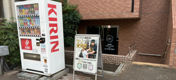 そうすると右手に自動販売機が見えてきます。その自販機が立っているマンションの一階が「THE PERSONAL GYM 赤羽店」になります。