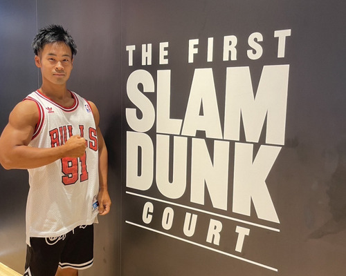 スラムダンクの文字背景の前でポーズしている村石トレーナー