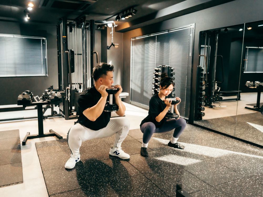 女性のお客様にスクワット指導を行うTHE PERSONAL GYM門前仲町店のトレーナーの様子