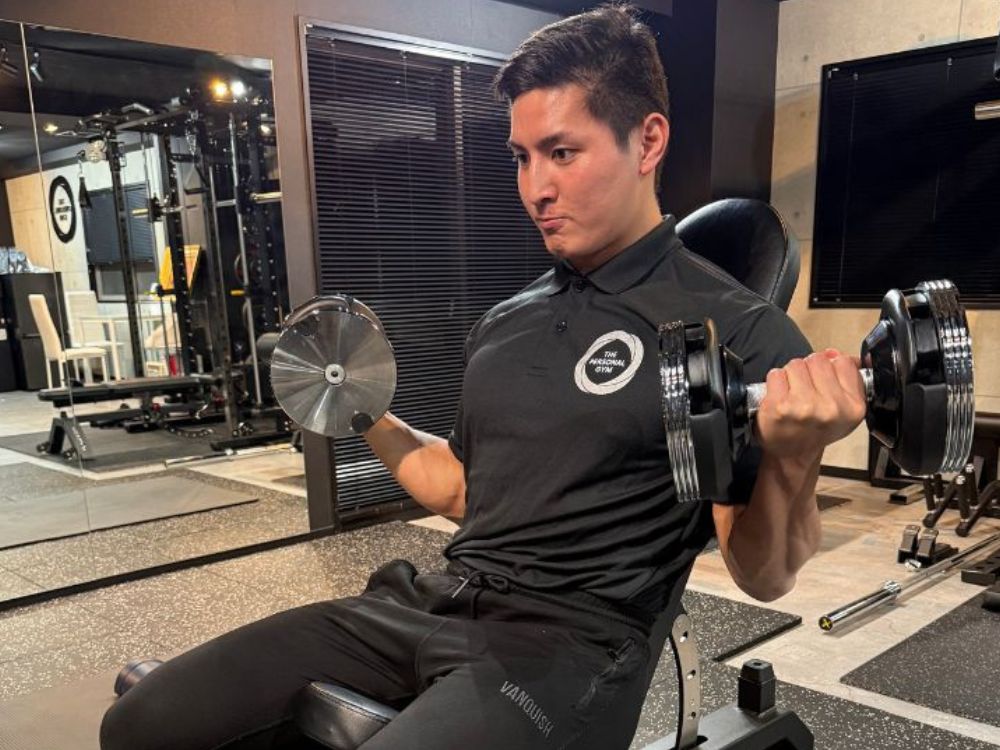 THE PERSONAL GYM門前仲町店で、初心者の方にも分かりやすくダンベルカールを行うパーソナルトレーナー小泉隼人。正しいフォームを意識したトレーニングの様子。