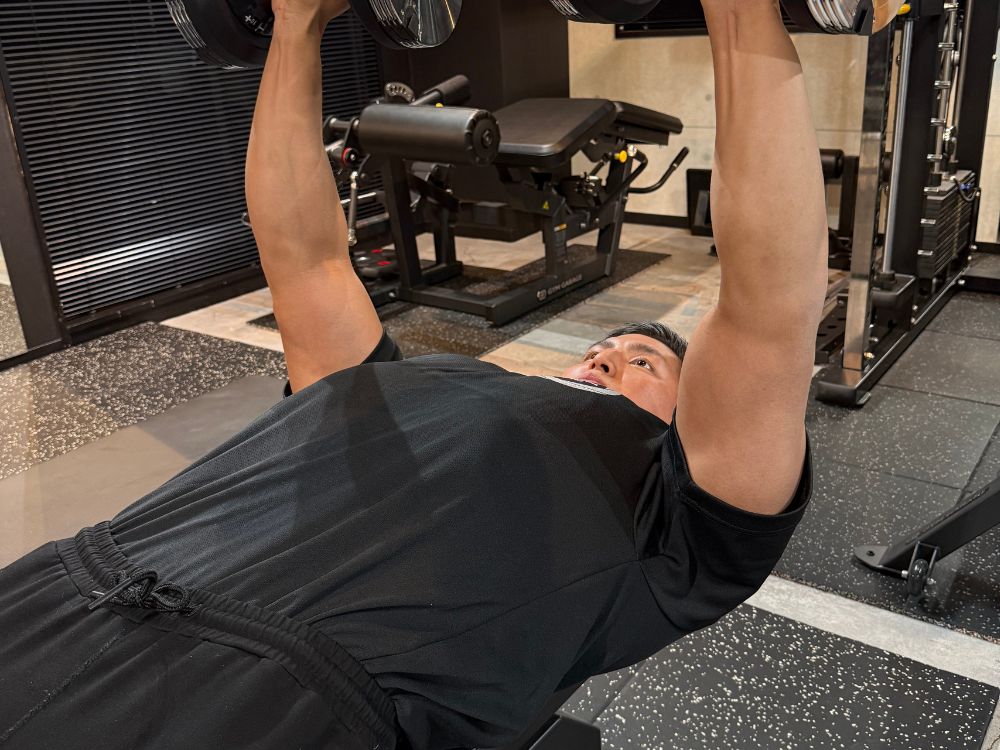 THE PERSONAL GYM門前仲町店で、ダンベルプレスを行いながらトレーニングを実演するパーソナルトレーナー小泉隼人。初心者の方にも分かりやすいフォームを意識している様子。