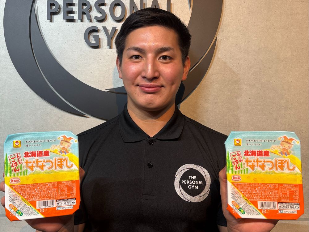 小泉トレーナーがパックご飯を持ちながら食事指導を説明している様子。江東区・門前仲町でパーソナルトレーニングが受けられるTHE PERSONAL GYM門前仲町店の食事サポート紹介。