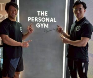 トレーナーとお客様がTHE PERSONAL GYM板橋店のロゴの前でポーズしている様子