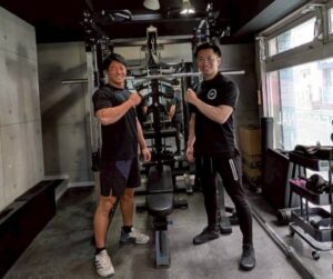 トレーナーとお客様がTHE PERSONAL GYM板橋店ANNEXのマシンの前でポーズしている様子