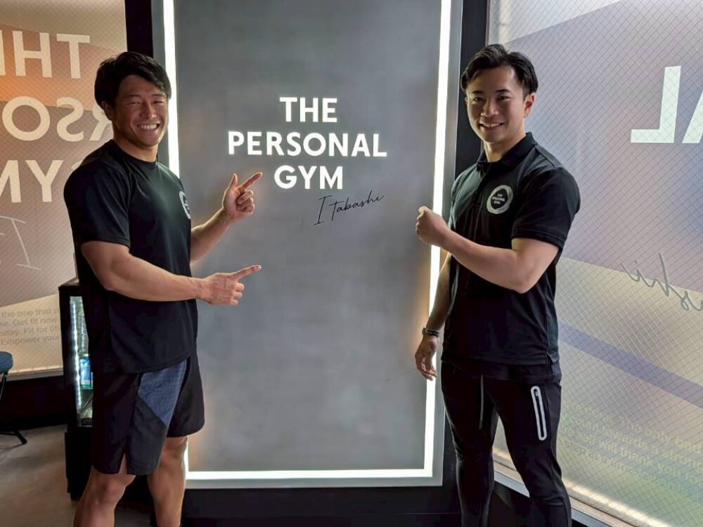 トレーナーとお客様がTHE PERSONAL GYM板橋店のロゴの前でポーズしている様子