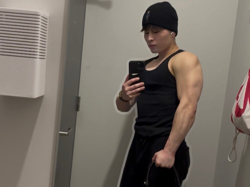 前田トレーナーのタンクトップ姿で鏡の前で写真を撮っている写真。