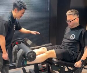 門前仲町のパーソナルジムでトレーナーがレッグエクステンションを指導し脚トレーニングをサポートしている様子