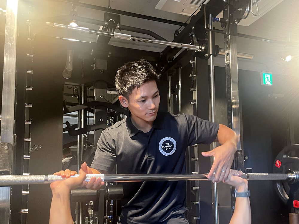 THE PERSONAL GYM薬院店でトレーナーがお客様のベンチプレスフォームを確認している様子
