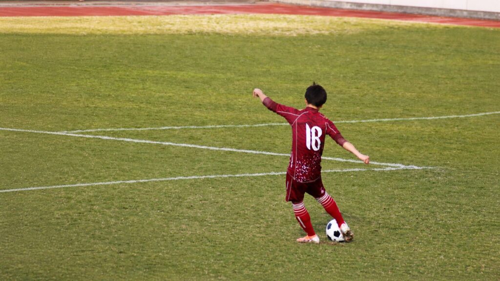 サッカーでボールを蹴る稲垣トレーナーの後ろ姿